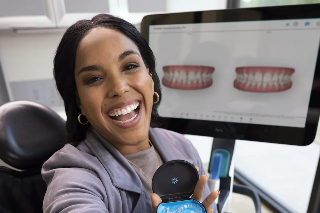 A hand holding a clear Invisalign aligner tray in front of a smiling patient